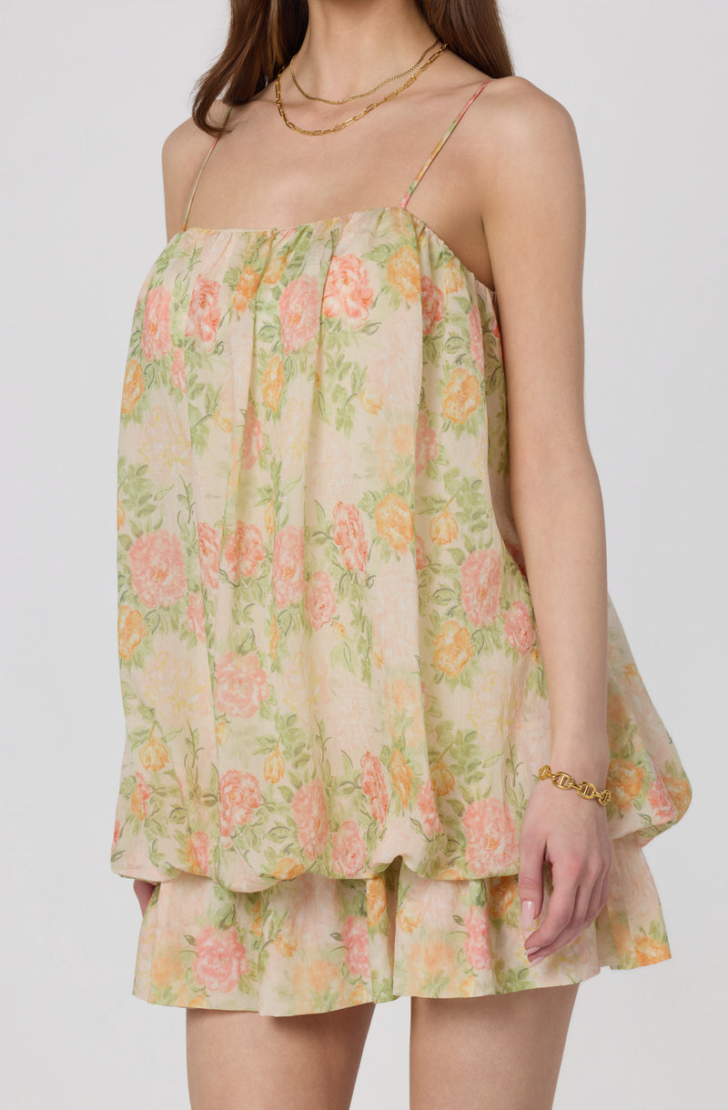 Woman wearing a floral pastel dress with spaghetti straps and layered shorts.