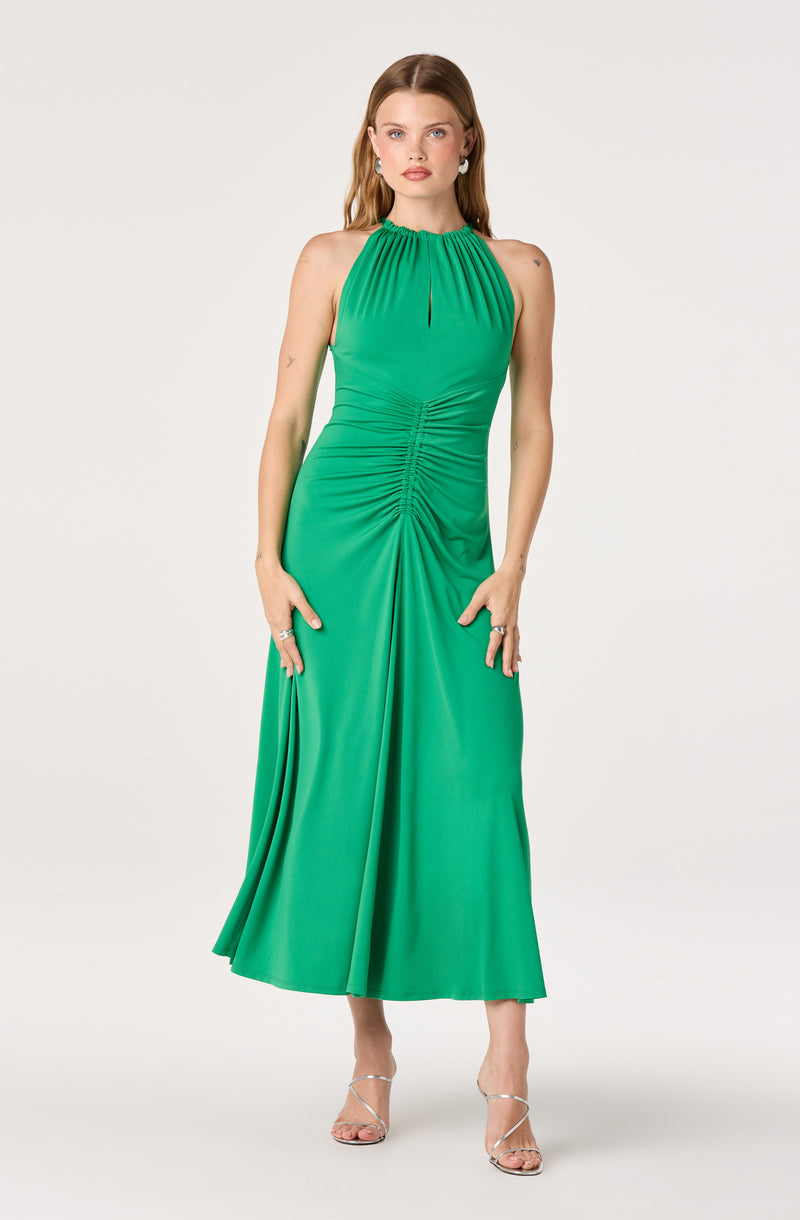 Woman wearing a green halter-neck, ruched, floor-length dress with a gathered waist and open-toe heels.