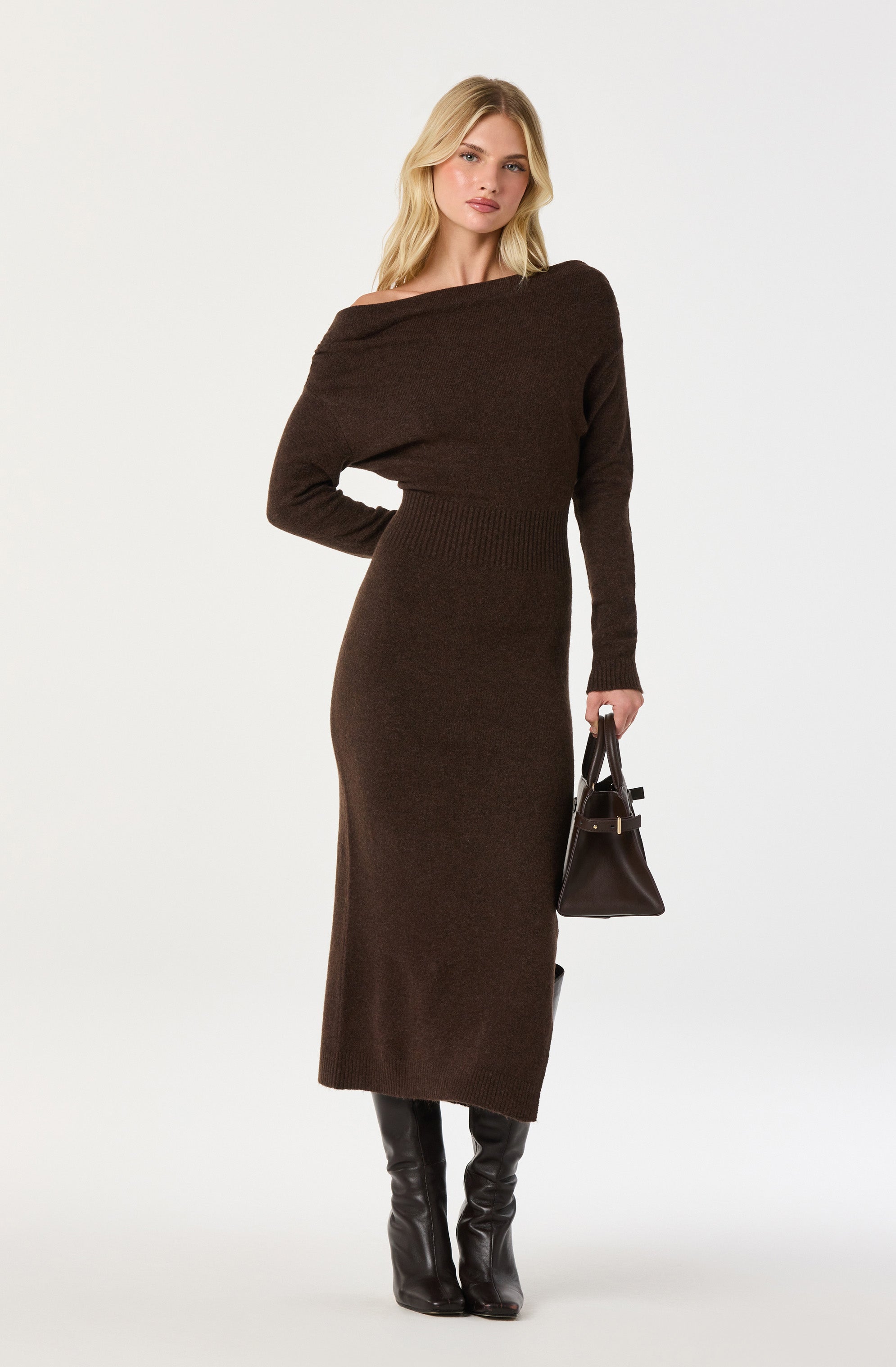 Brown off-shoulder knit dress with long sleeves and black knee-high boots, carrying a black handbag.