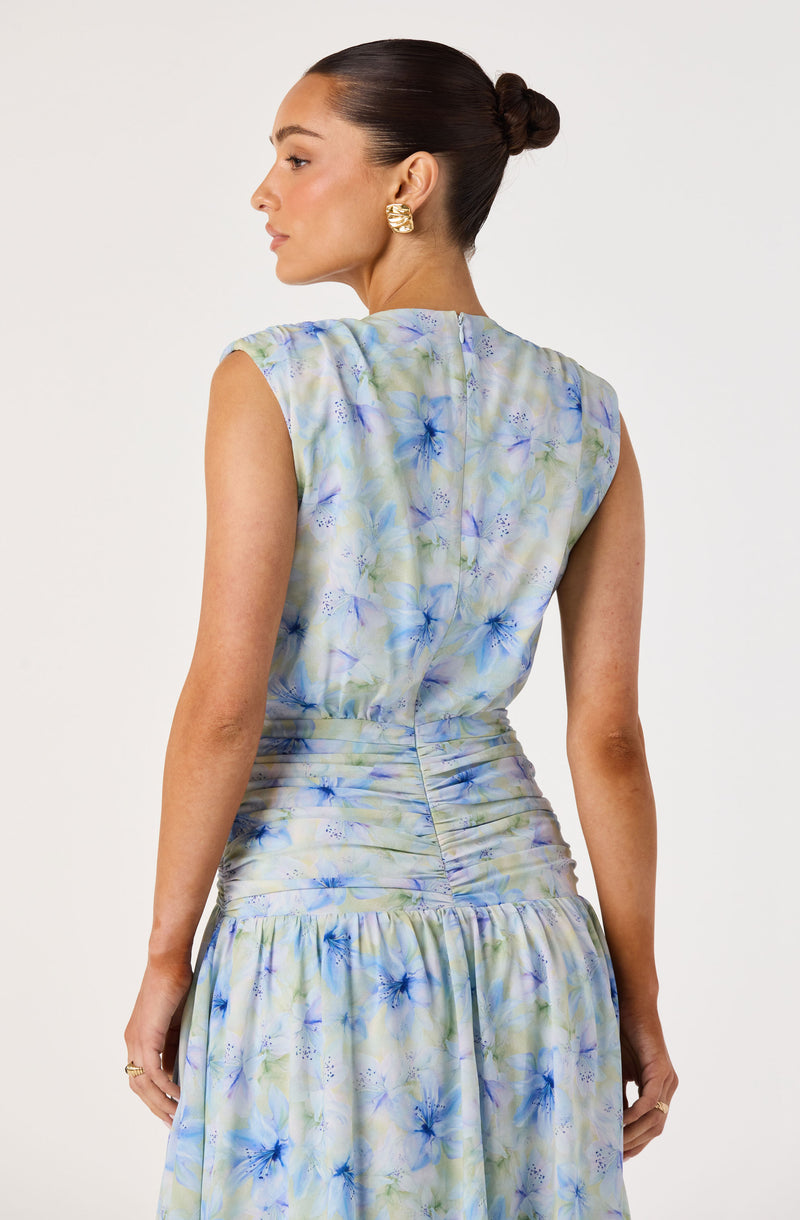 Woman wearing a sleeveless, pastel floral dress with ruched details at the waist and a ruffled hem.