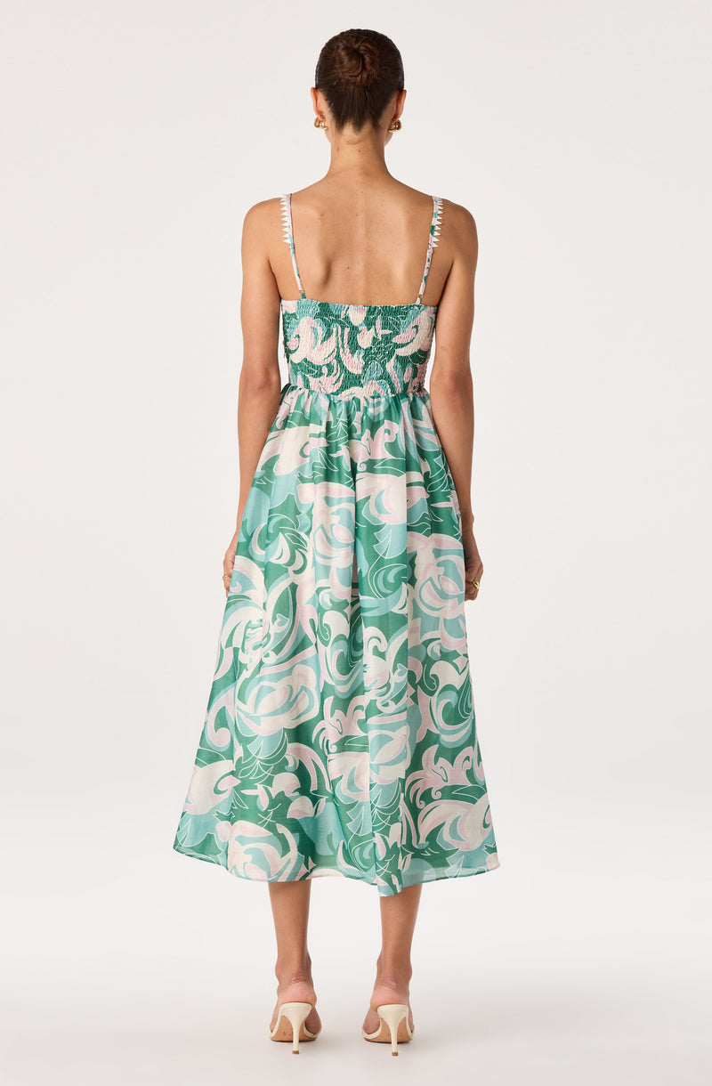 Back view of a woman in a flowy, patterned maxi dress with thin spaghetti straps.