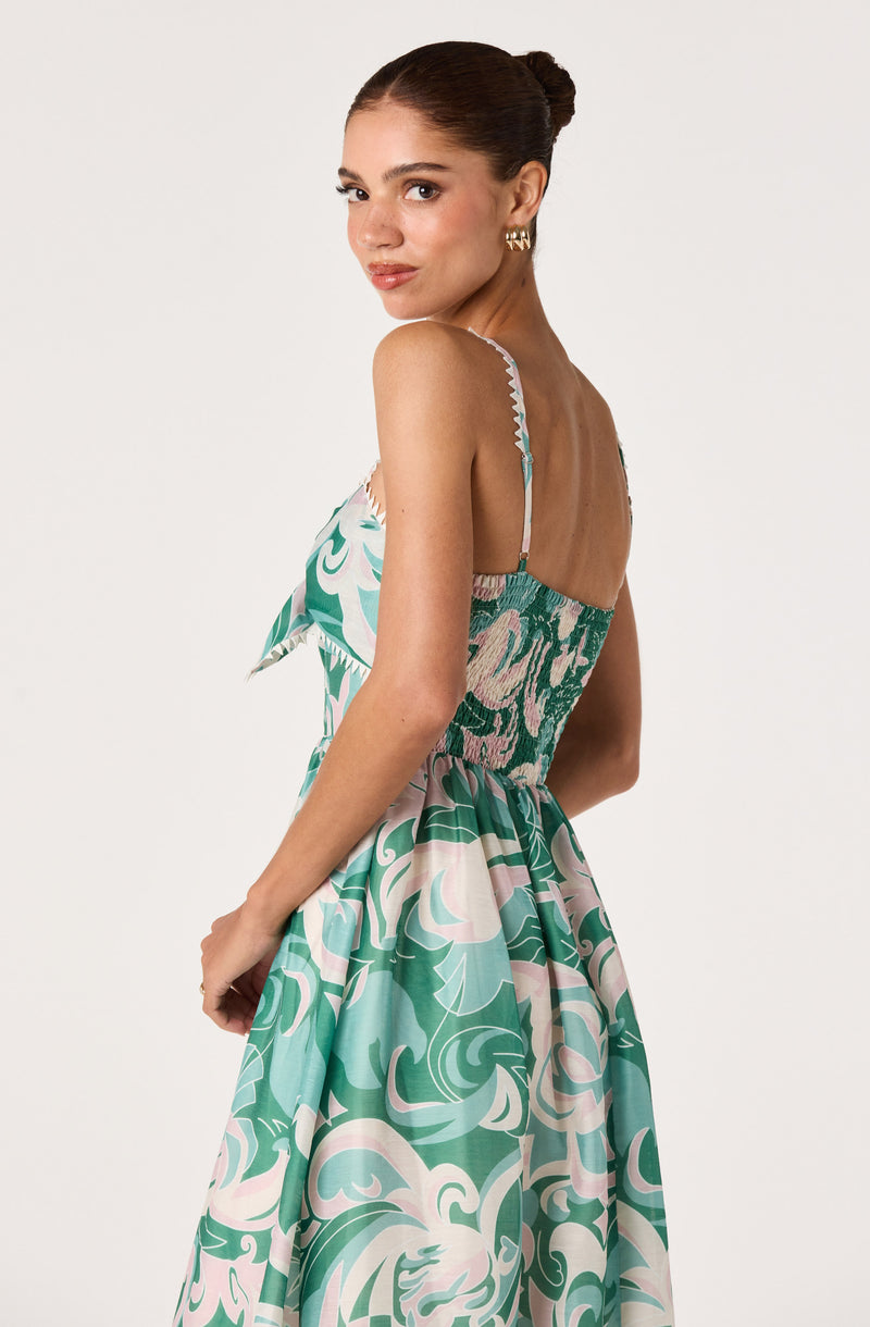 Woman wearing a sleeveless dress with floral and swirl patterns in green, blue, and pink.
