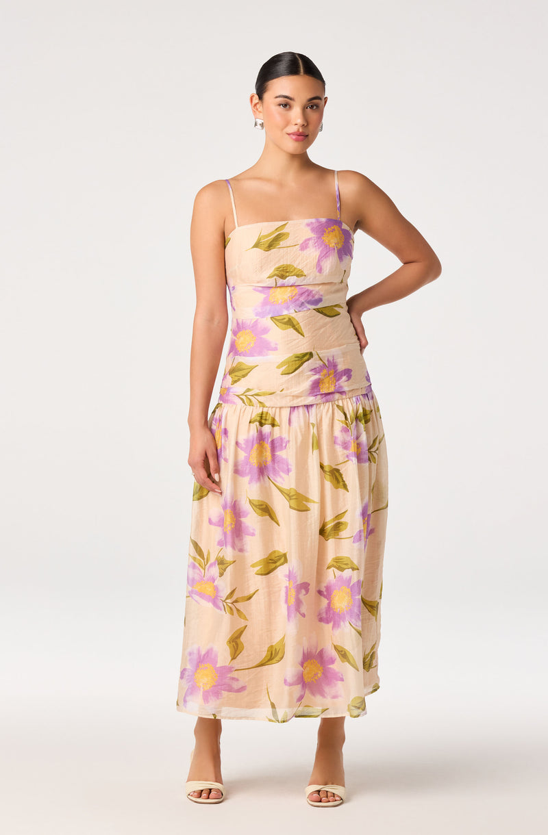 Woman in a floral beige dress with purple and yellow flowers and thin straps.