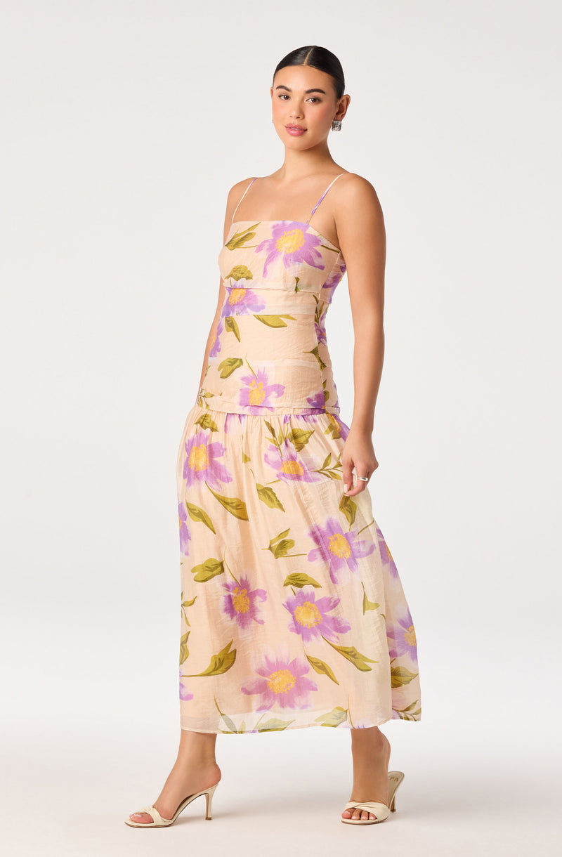Woman in a cream-colored, floral-print sleeveless evening dress with spaghetti straps and a sheer, flowing skirt.