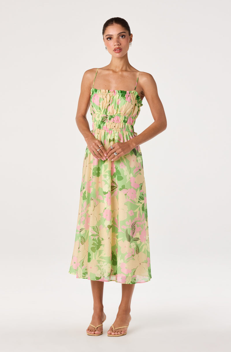 Woman wearing a sleeveless, floral summer dress with spaghetti straps and a gathered waist.