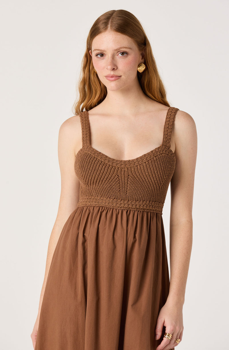 Woman in a brown dress with a knitted bodice and gathered skirt, gold earrings, and a ring.