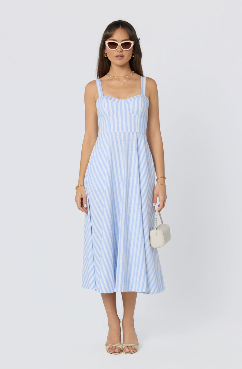 Woman wearing a light blue and white striped sleeveless midi dress, paired with white sunglasses, gold jewelry, and beige heels.