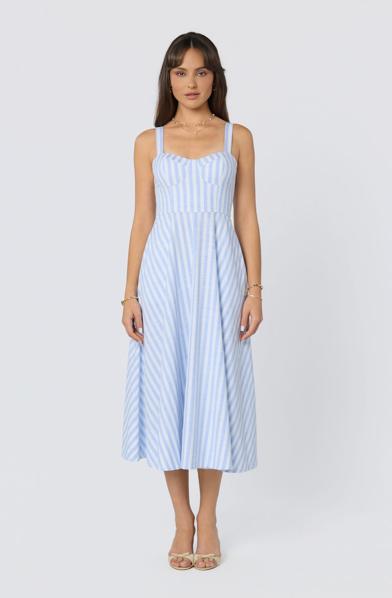 Woman wearing a sleeveless, light blue and white striped midi dress with wide straps.