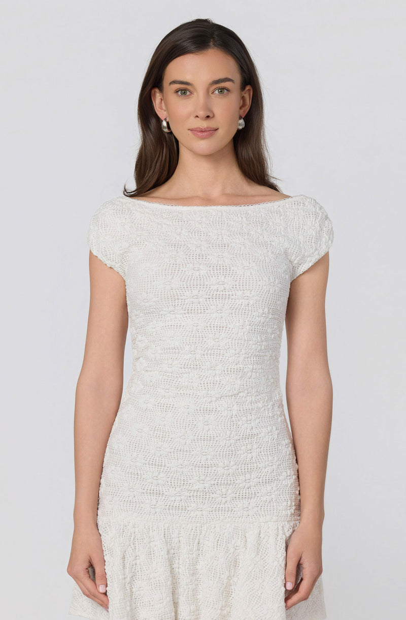 Woman in a white, textured, short-sleeve dress with a ruffled hem.