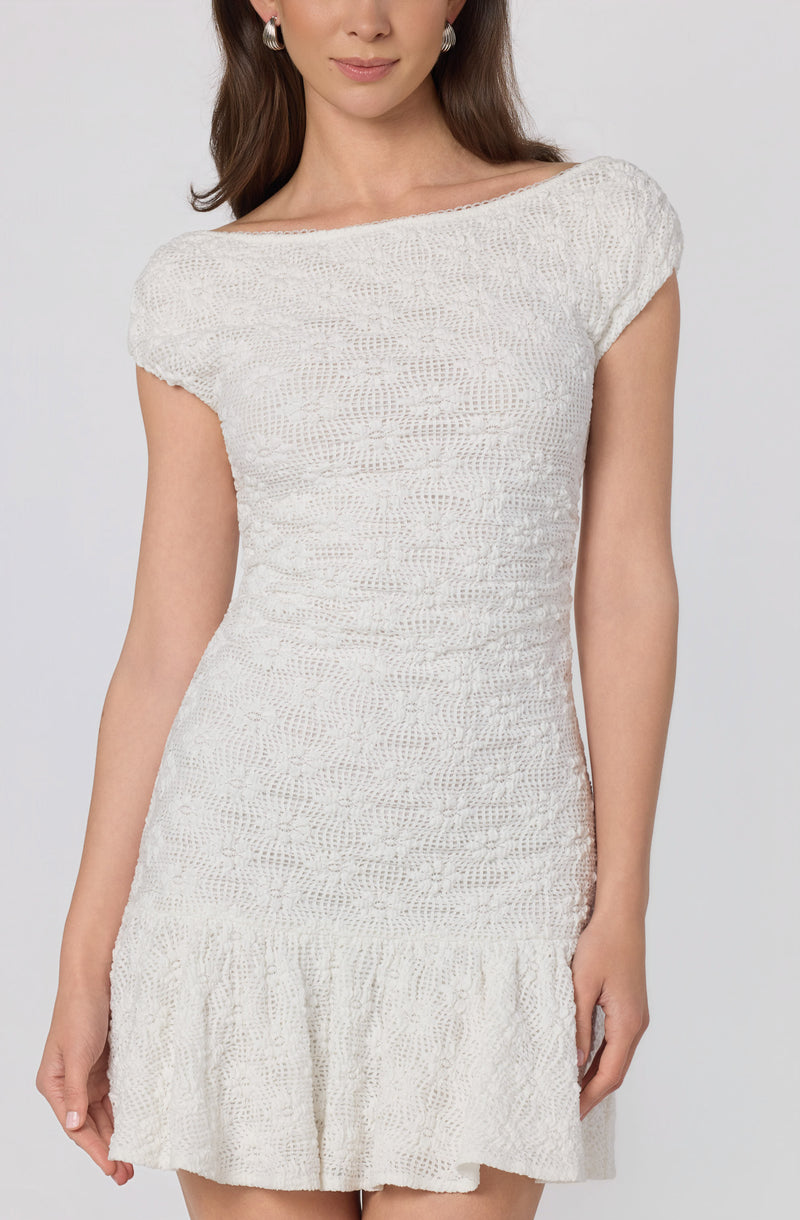 Woman wearing a white, short-sleeved, knitted dress with a ruffled hem at the bottom.