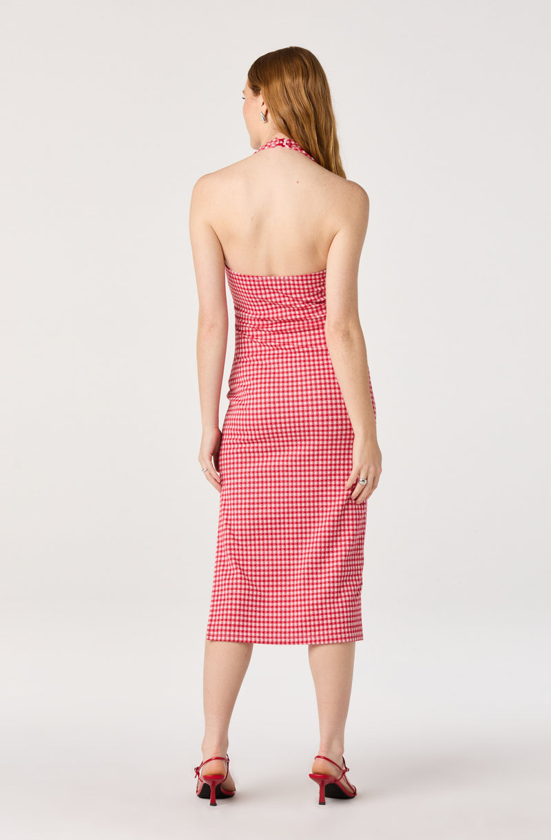 Back view of a woman wearing a sleeveless red and white checkered halter dress and red high-heeled shoes.