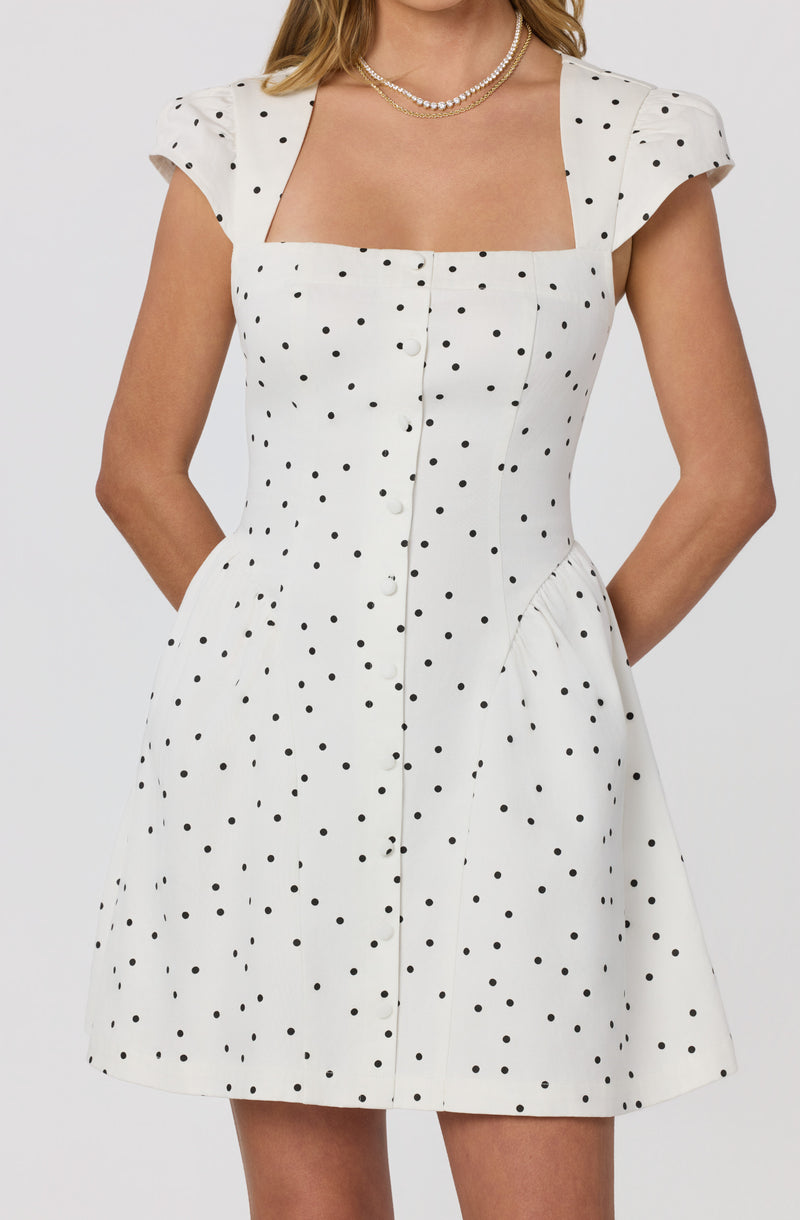 White dress with black polka dots, short puff sleeves, square neckline, and front button details.