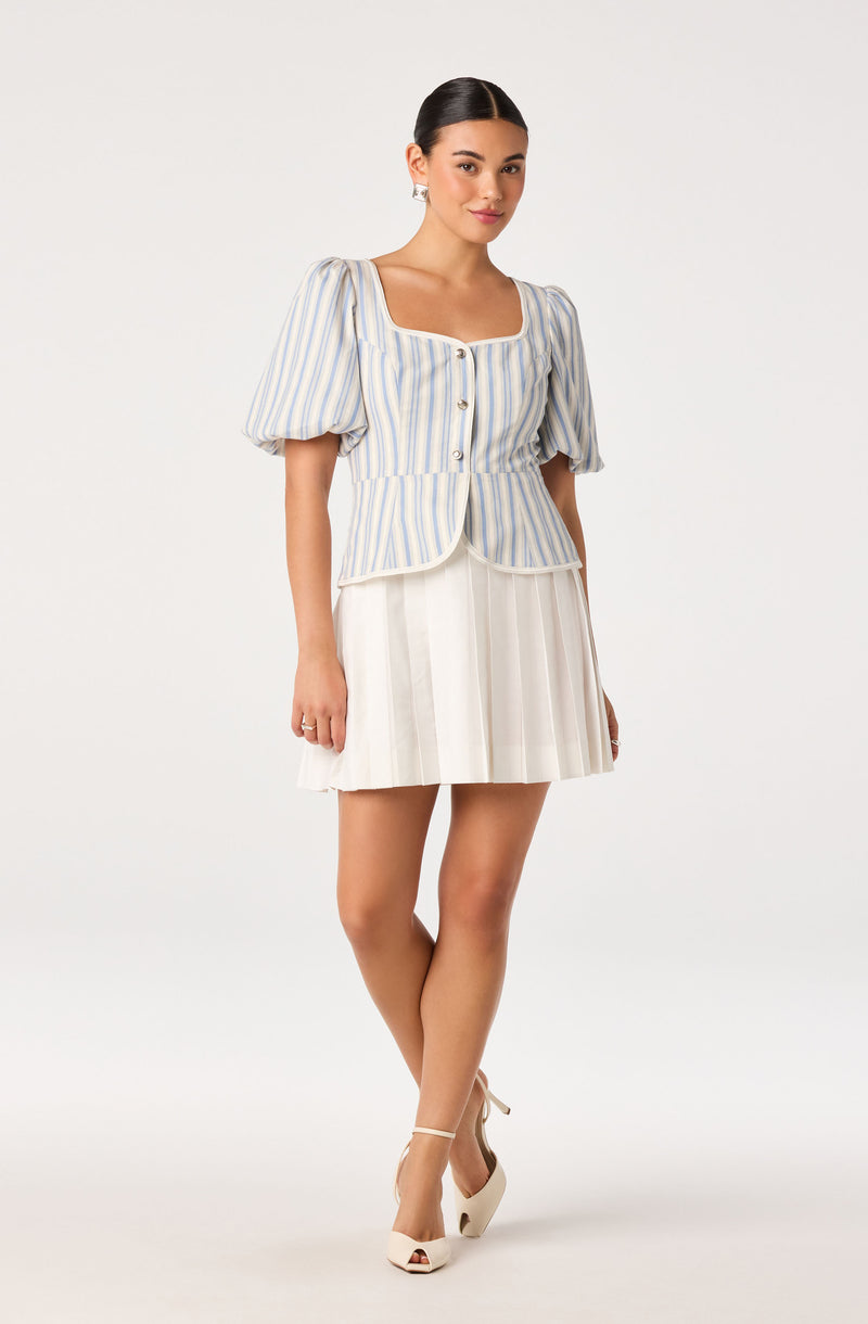 Woman in a light striped blouse with puffed sleeves and a pleated white skirt.