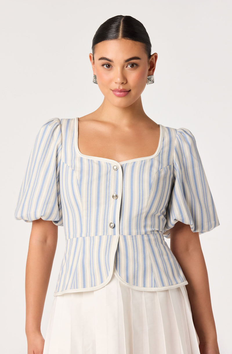 Woman wearing a light blue and beige striped blouse with puffed sleeves and silver buttons.