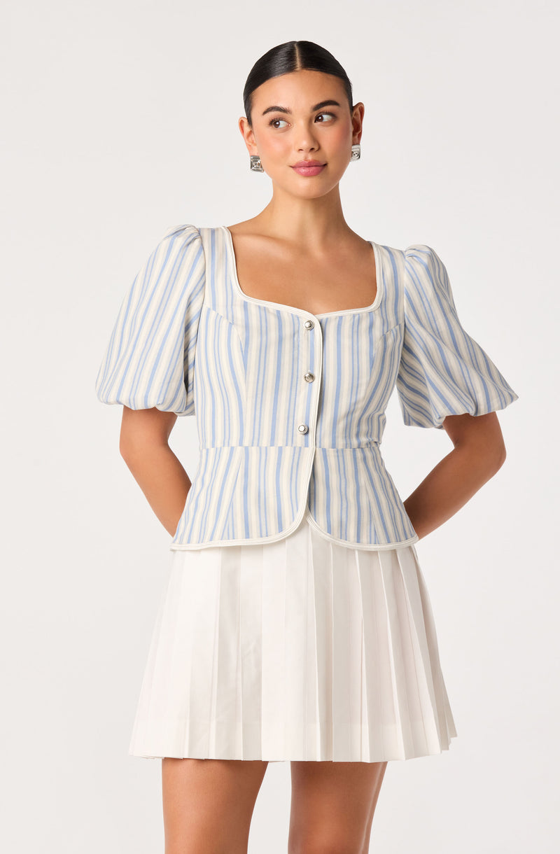 Woman in a light blue and white striped puff-sleeve top with buttons, paired with a white pleated skirt.