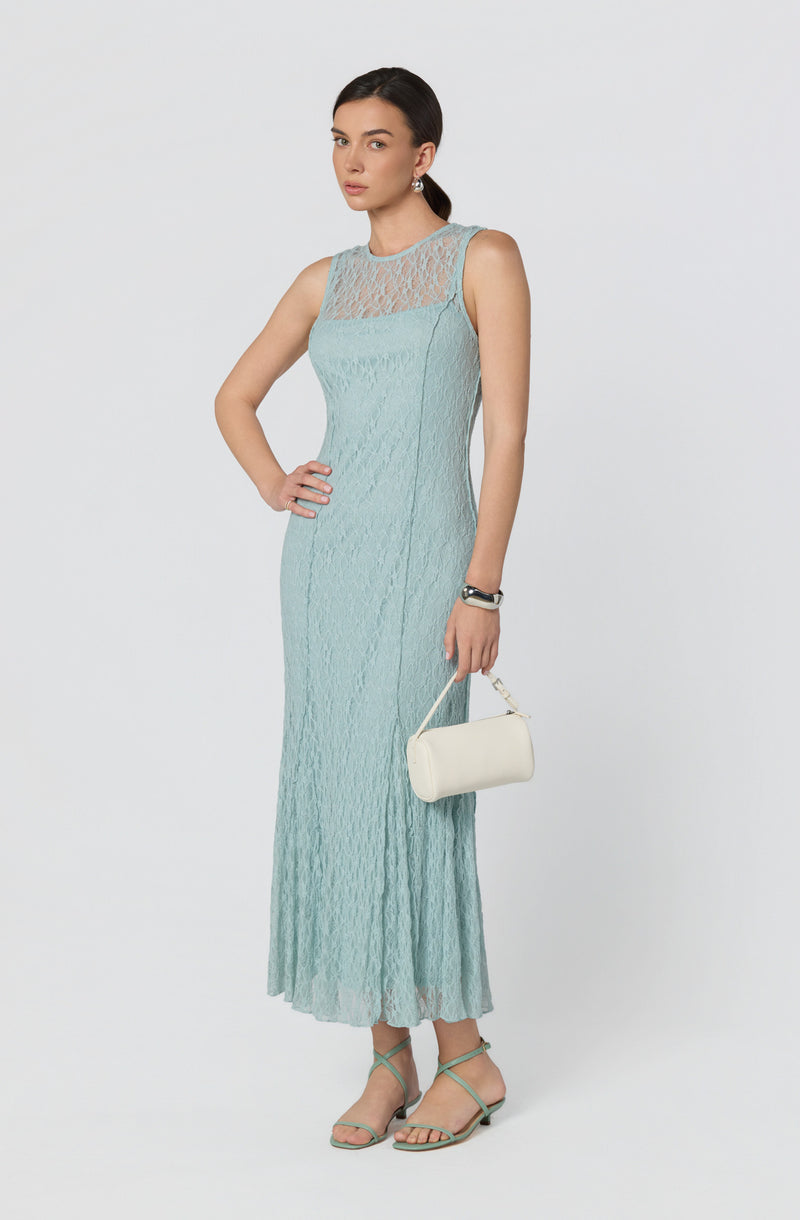 Woman wearing a pale blue, sleeveless lace maxi dress with a sheer lace neckline, paired with teal strappy heels, silver earrings, and holding a white clutch.
