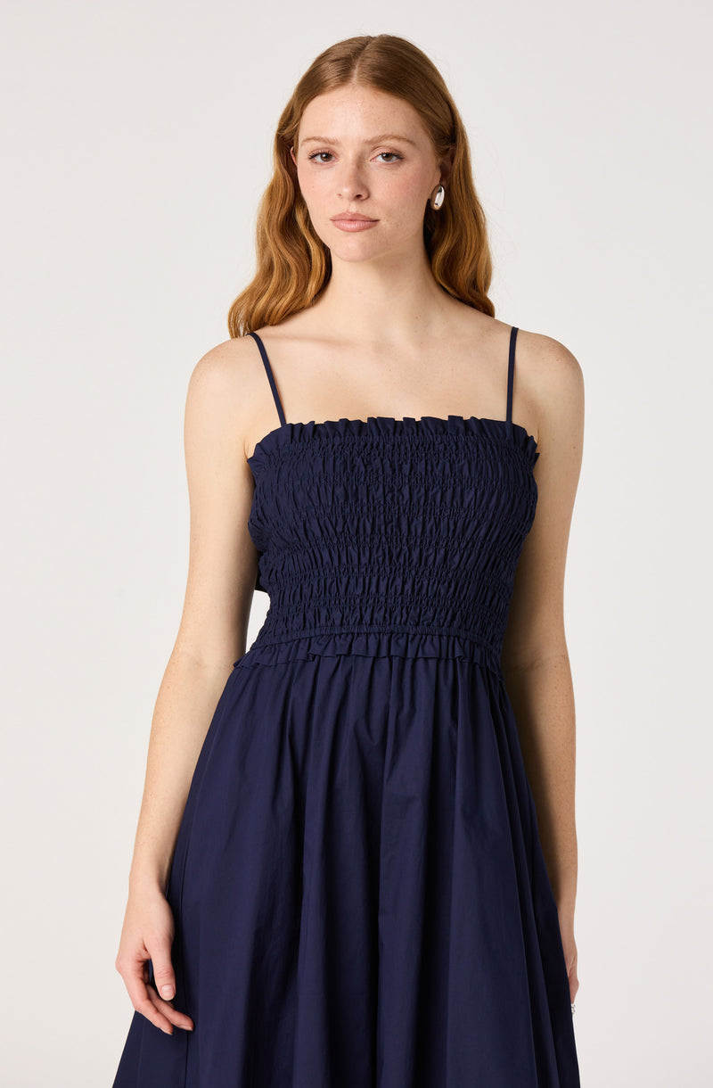 Woman wearing a navy blue dress with a shirred bodice and thin spaghetti straps.