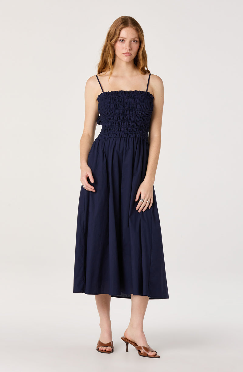 Woman in a navy blue dress with spaghetti straps and a gathered top, paired with brown heeled sandals.