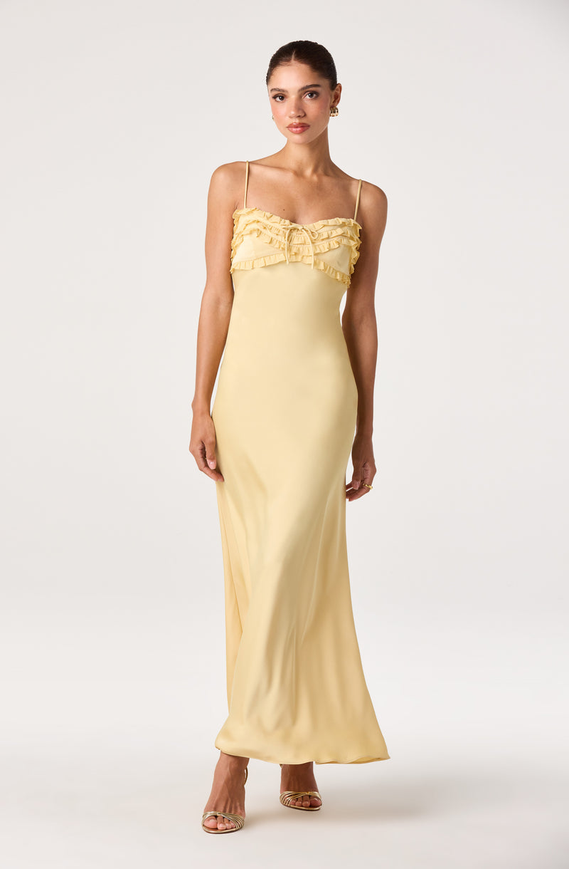 Woman wearing a long, light yellow dress with ruffled bodice and thin straps.