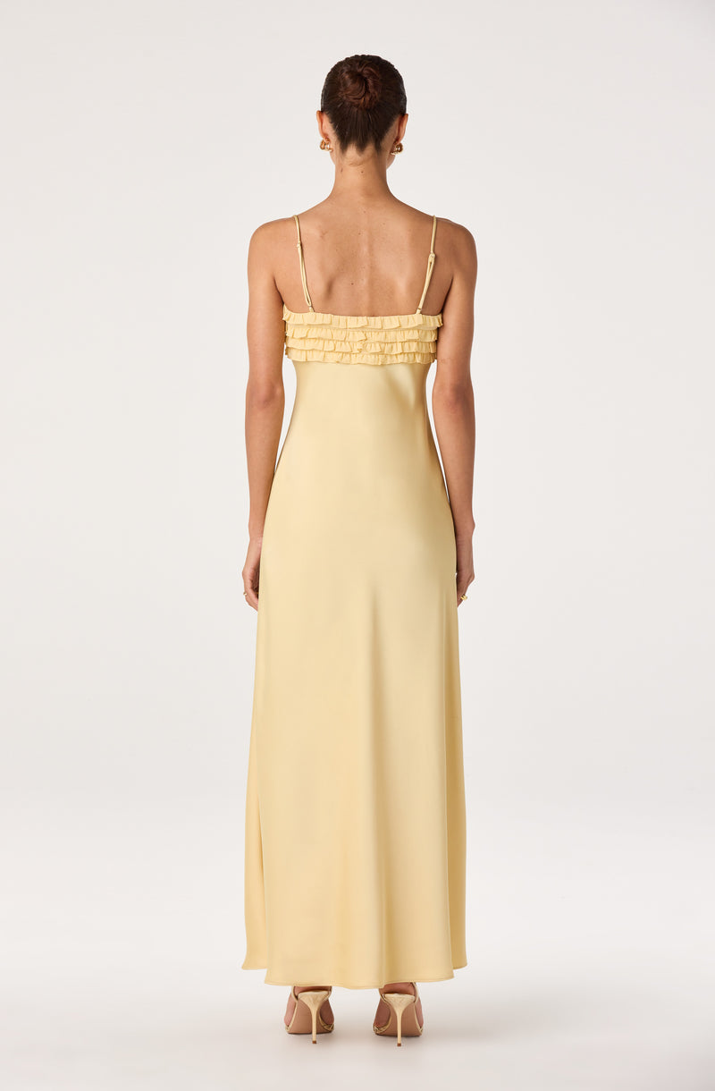 Back view of a woman wearing a long, pale yellow dress with ruffled bandeau top and spaghetti straps.