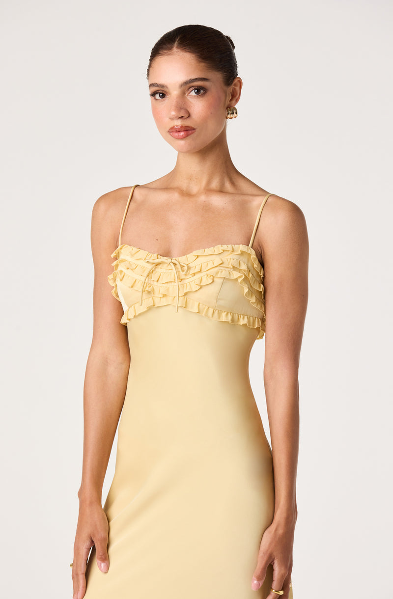 Girl wearing a yellow slip dress with ruffled detail and spaghetti straps.