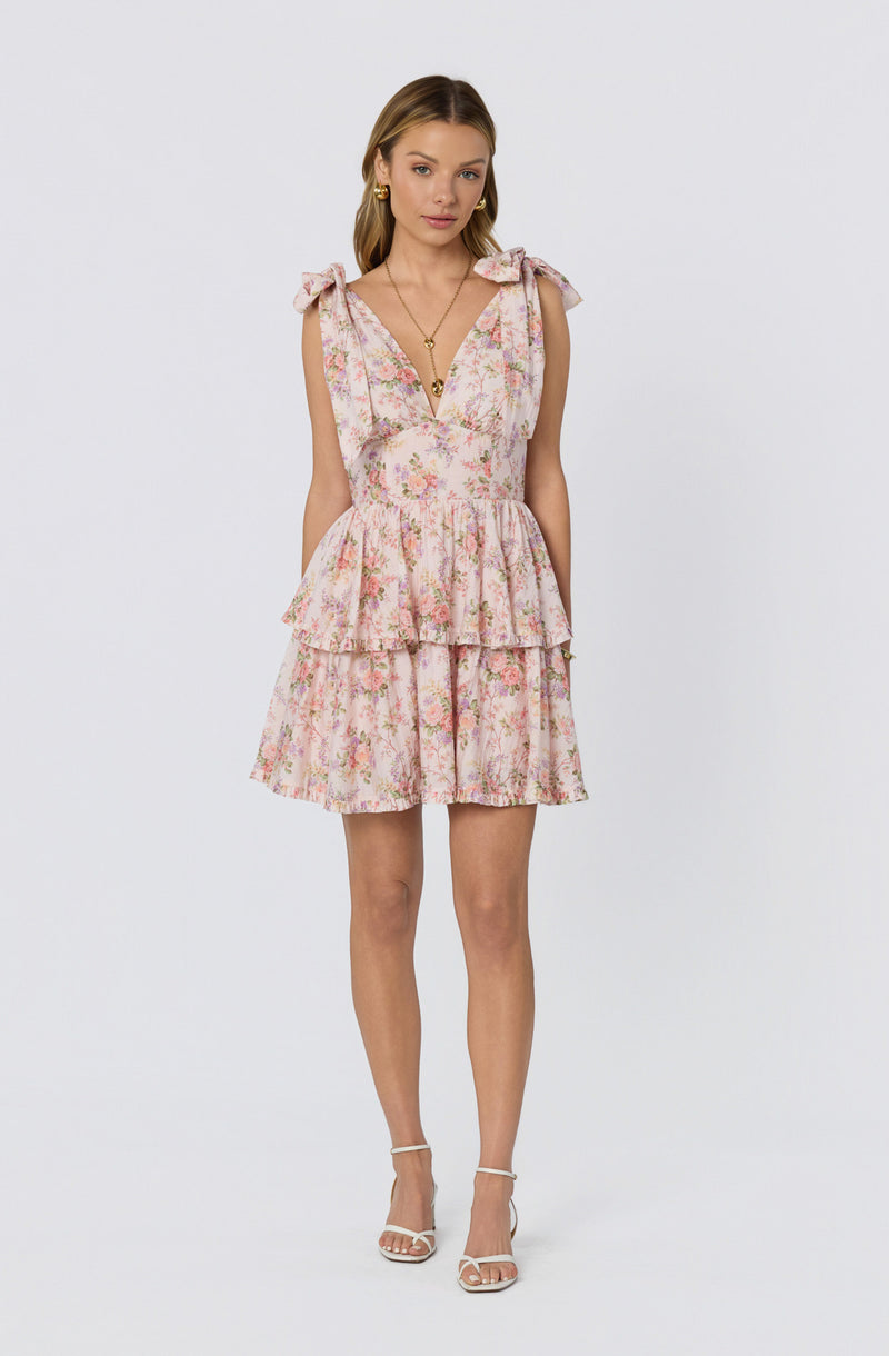 Woman wearing a pink floral dress with ruffled layers and tie-shoulder bows.