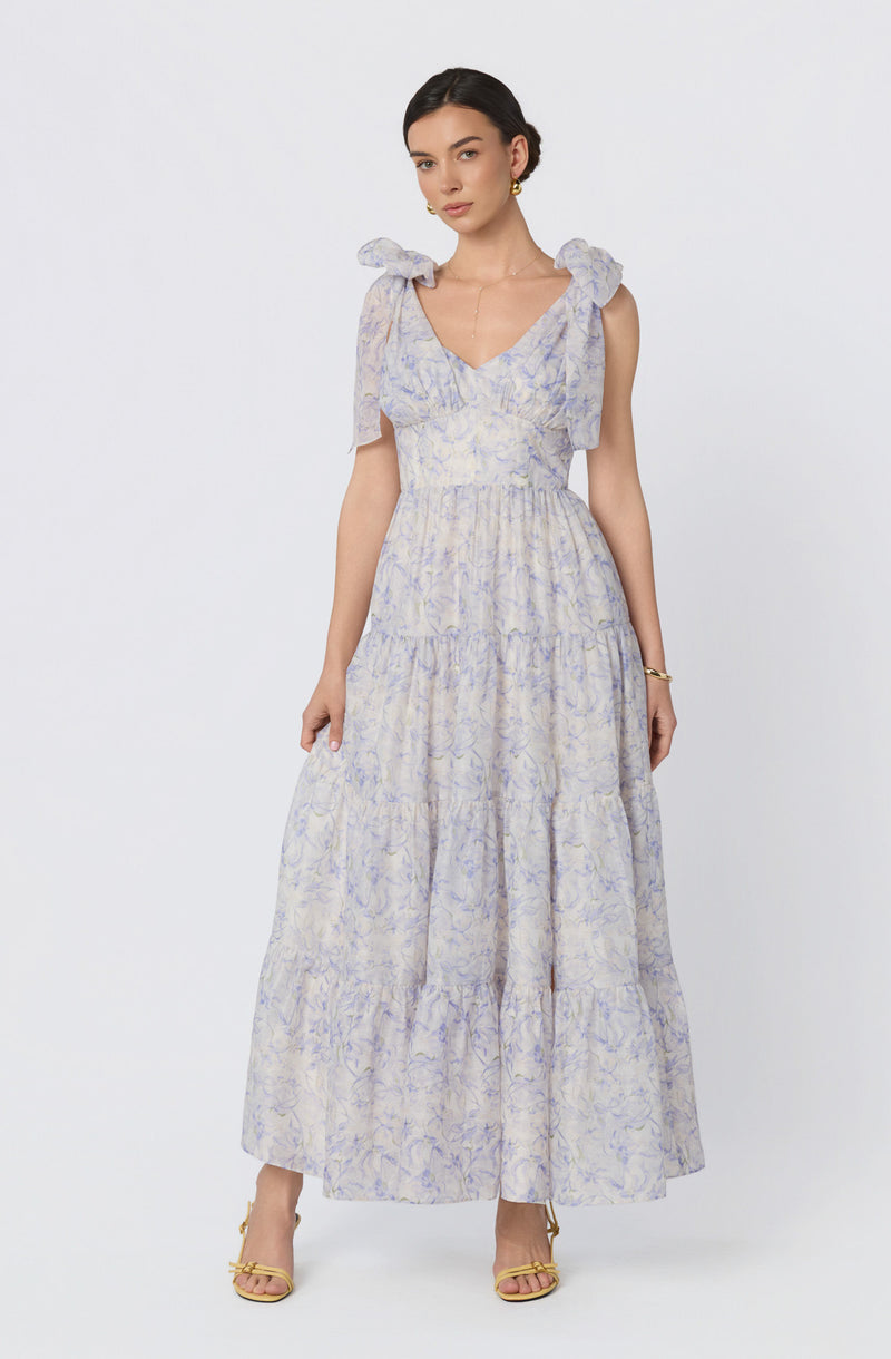 Woman wearing a flowy, lavender and white floral dress with ruffled shoulder straps and yellow heels.