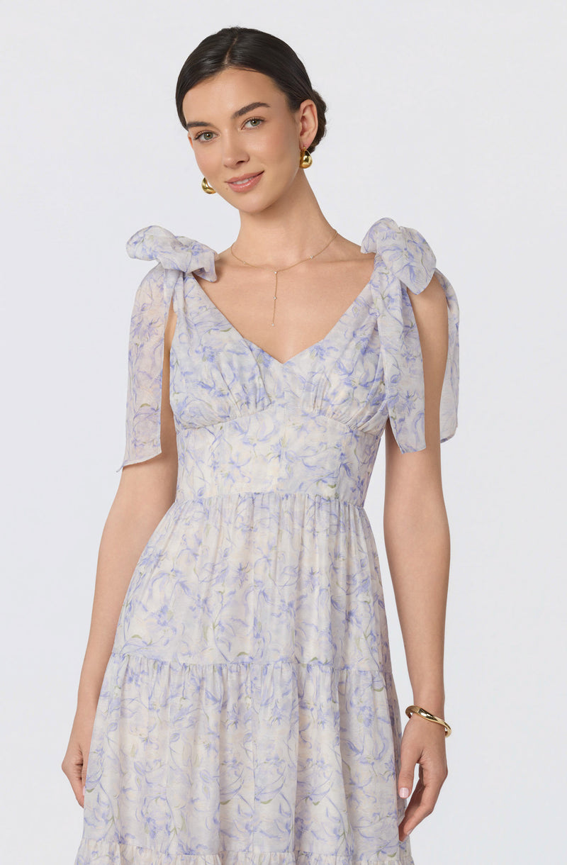 Woman in a light, floral-patterned dress with ruffled shoulder ties and a deep V neckline.