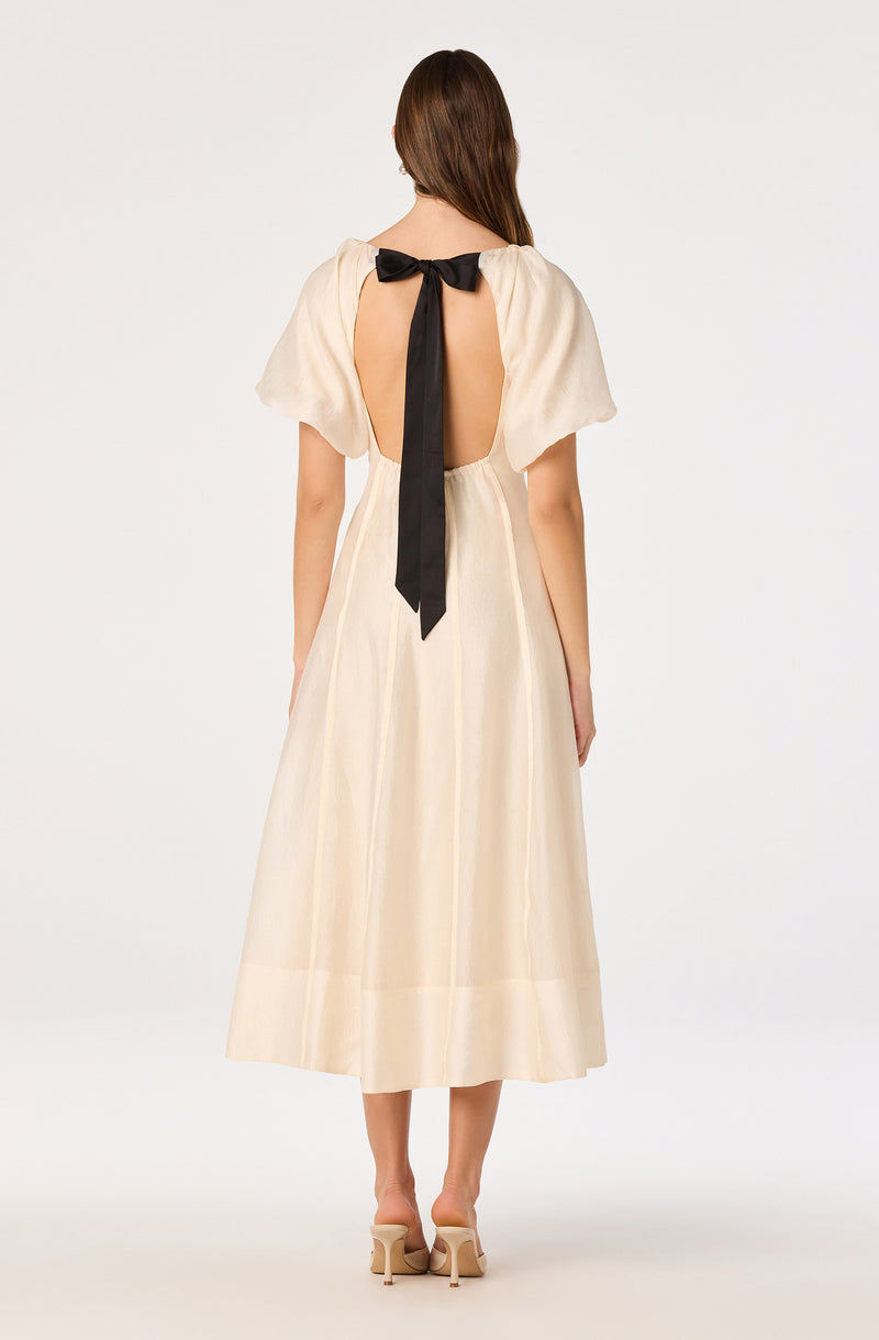 Cream-colored dress with short puff sleeves and an open back tied with a black bow.