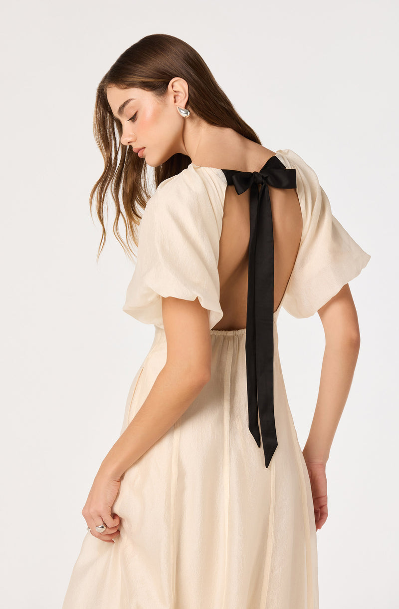 Woman wearing a cream dress with puff sleeves and a black ribbon tied at the back.