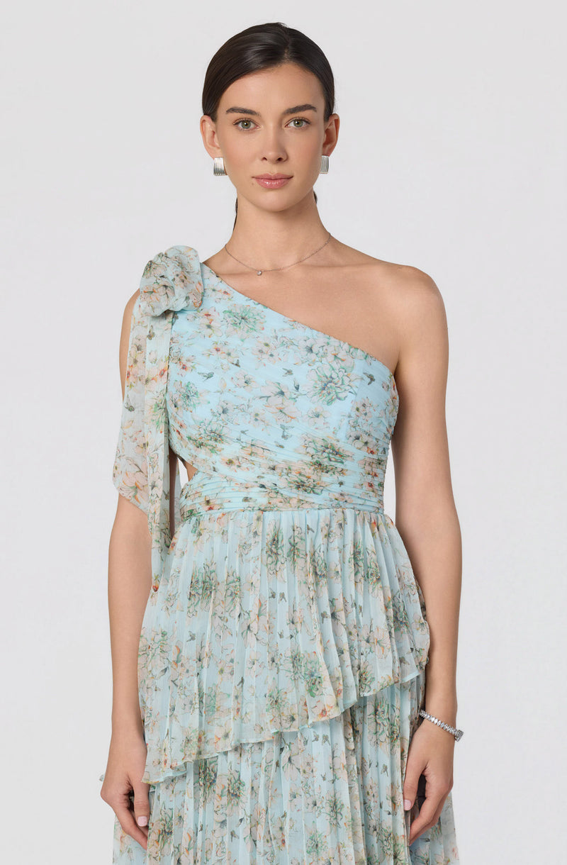 Woman wearing a one-shoulder dress with a floral pattern and a large bow on the shoulder.