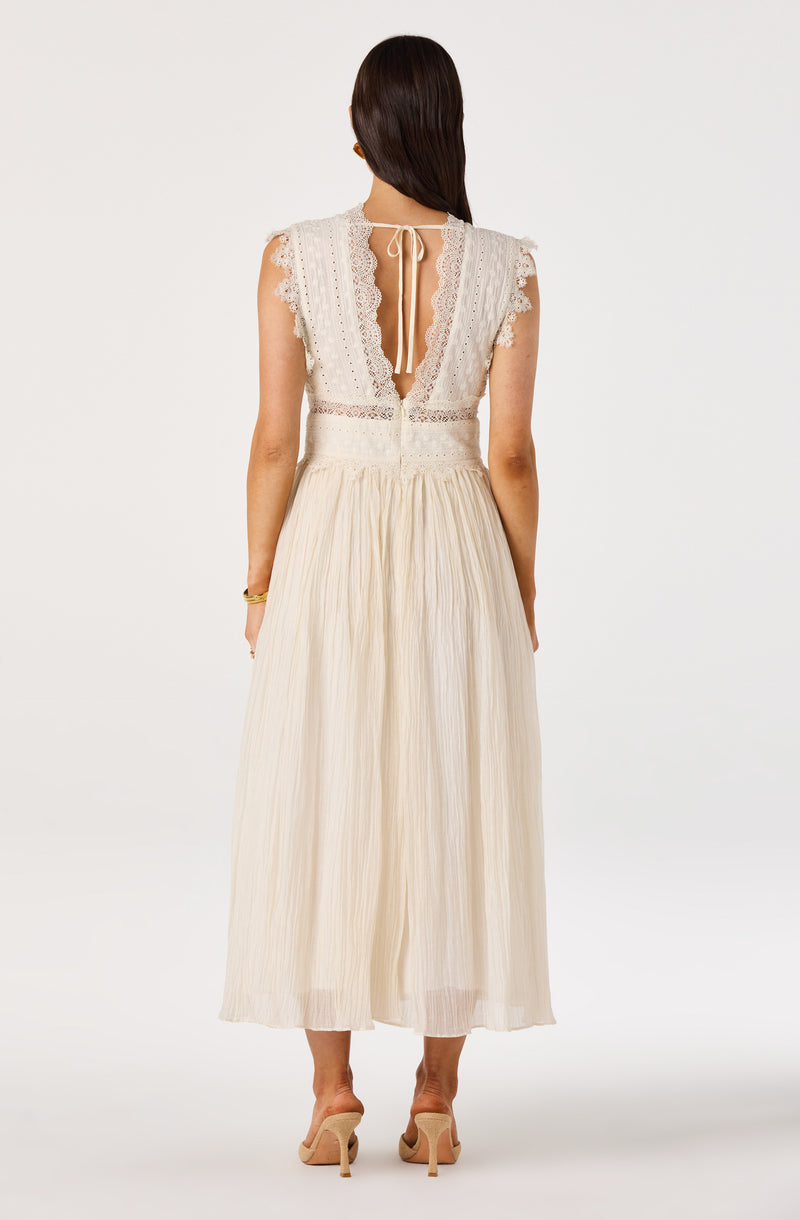Woman in cream lace top and long pleated skirt, back view, nude heels.