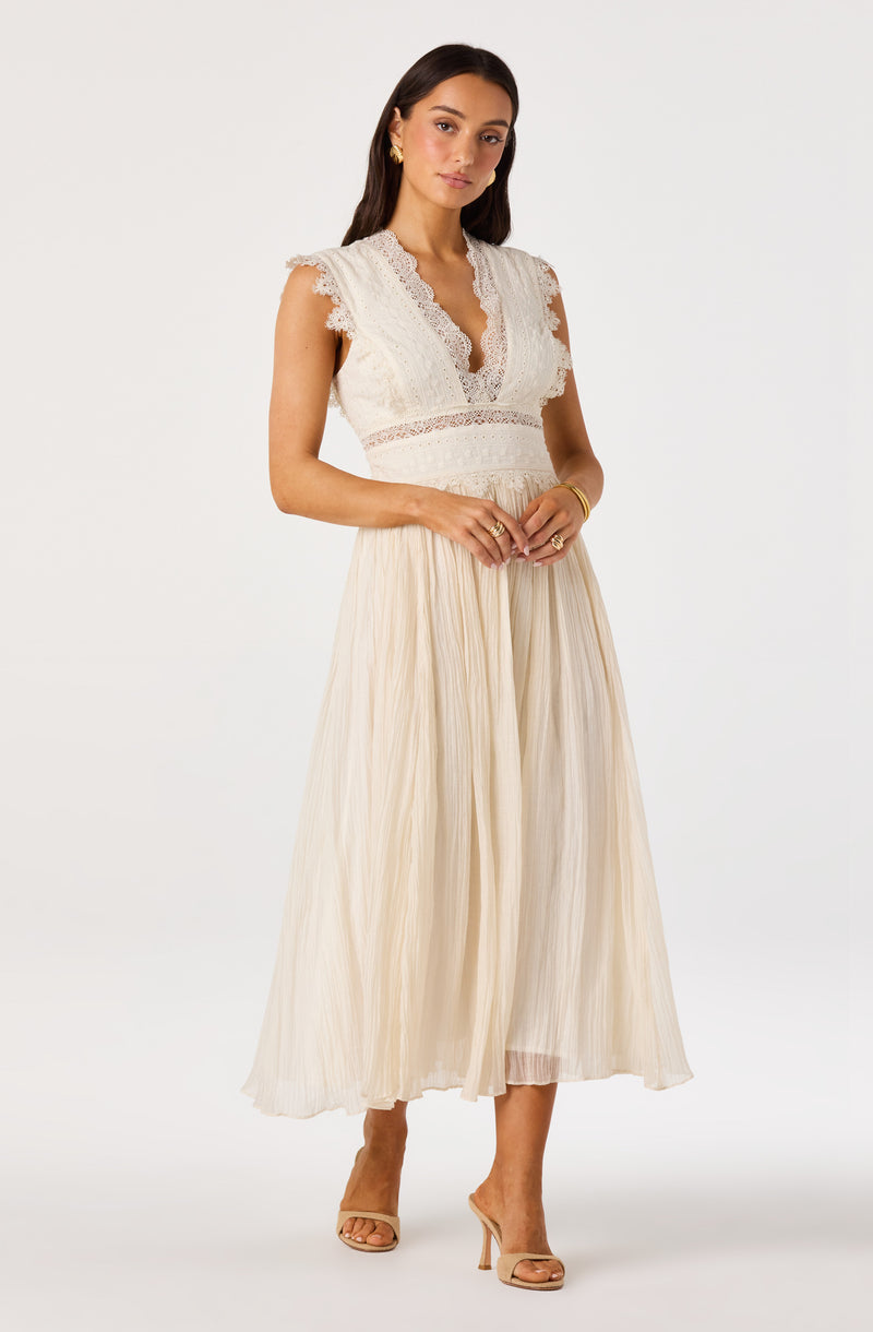 Woman in cream lace top with ruffled sleeves and a pleated, flowy cream skirt.