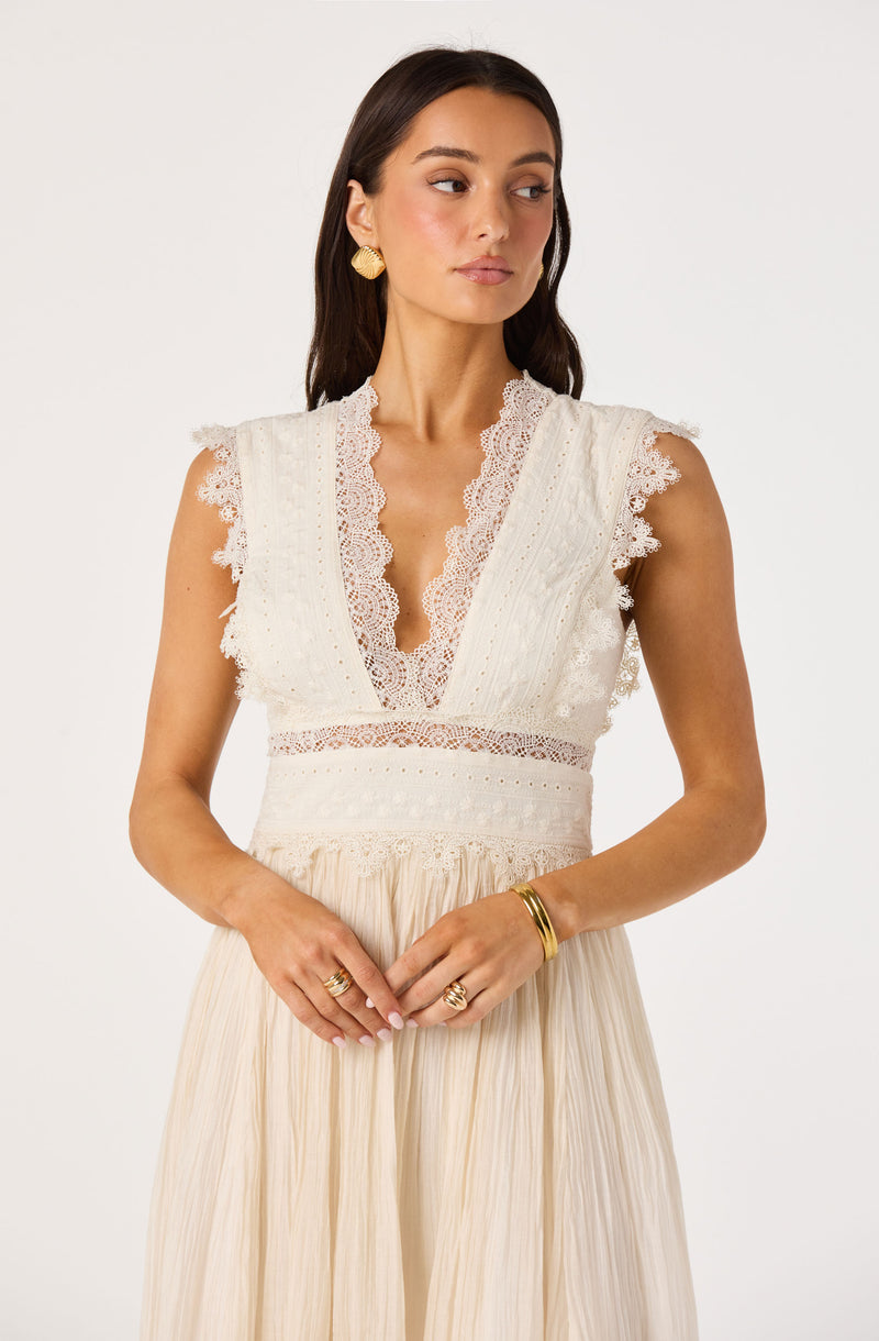 Woman wearing cream-colored dress with lace details and pleated skirt.