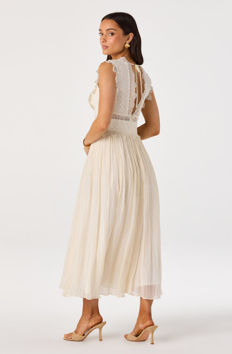 Woman in cream lace top and pleated midi skirt, beige heels.