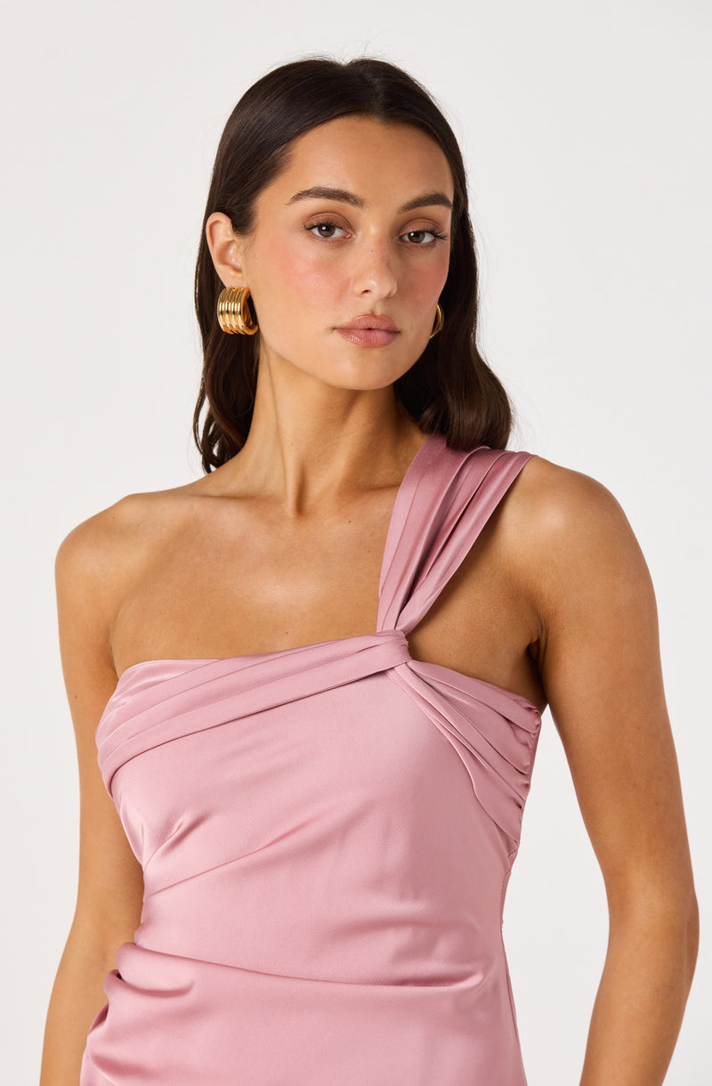 Woman in a pink satin one-shoulder dress with pleated detailing and gold hoop earrings.
