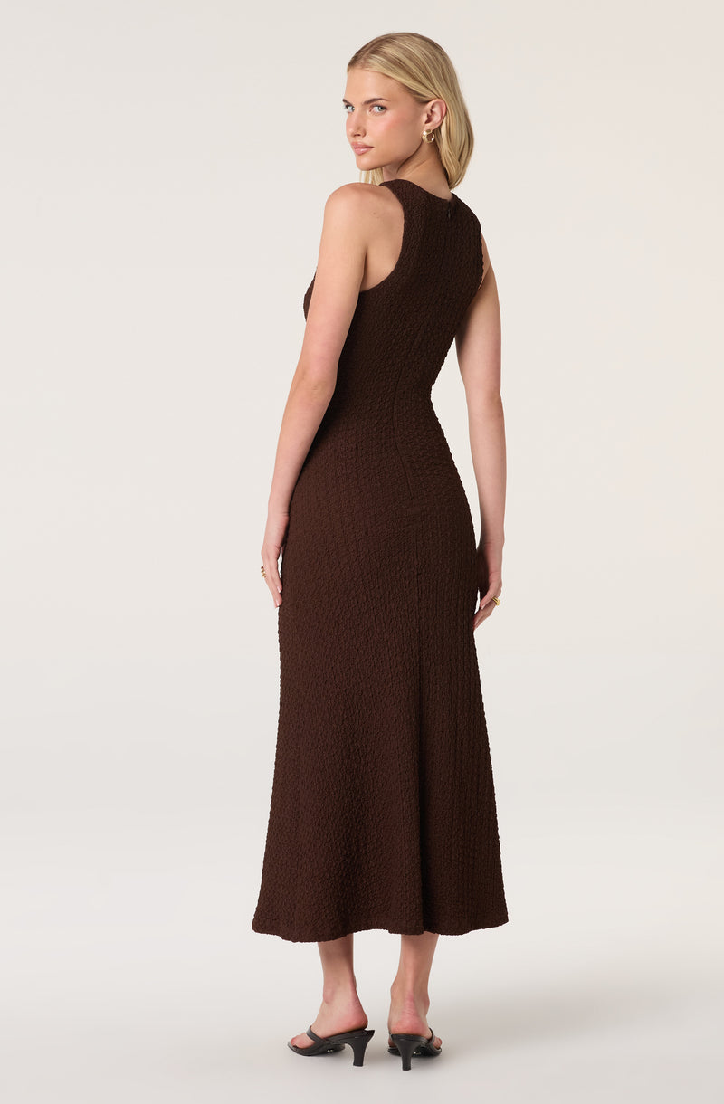 Woman in a sleeveless, textured, dark brown maxi dress with a fitted waist and a side slit.