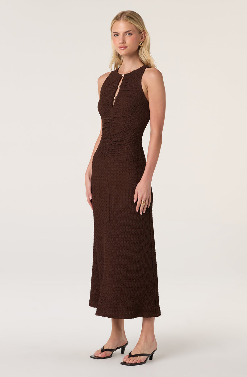 Woman in a brown sleeveless, textured, floor-length dress with a short front slit.