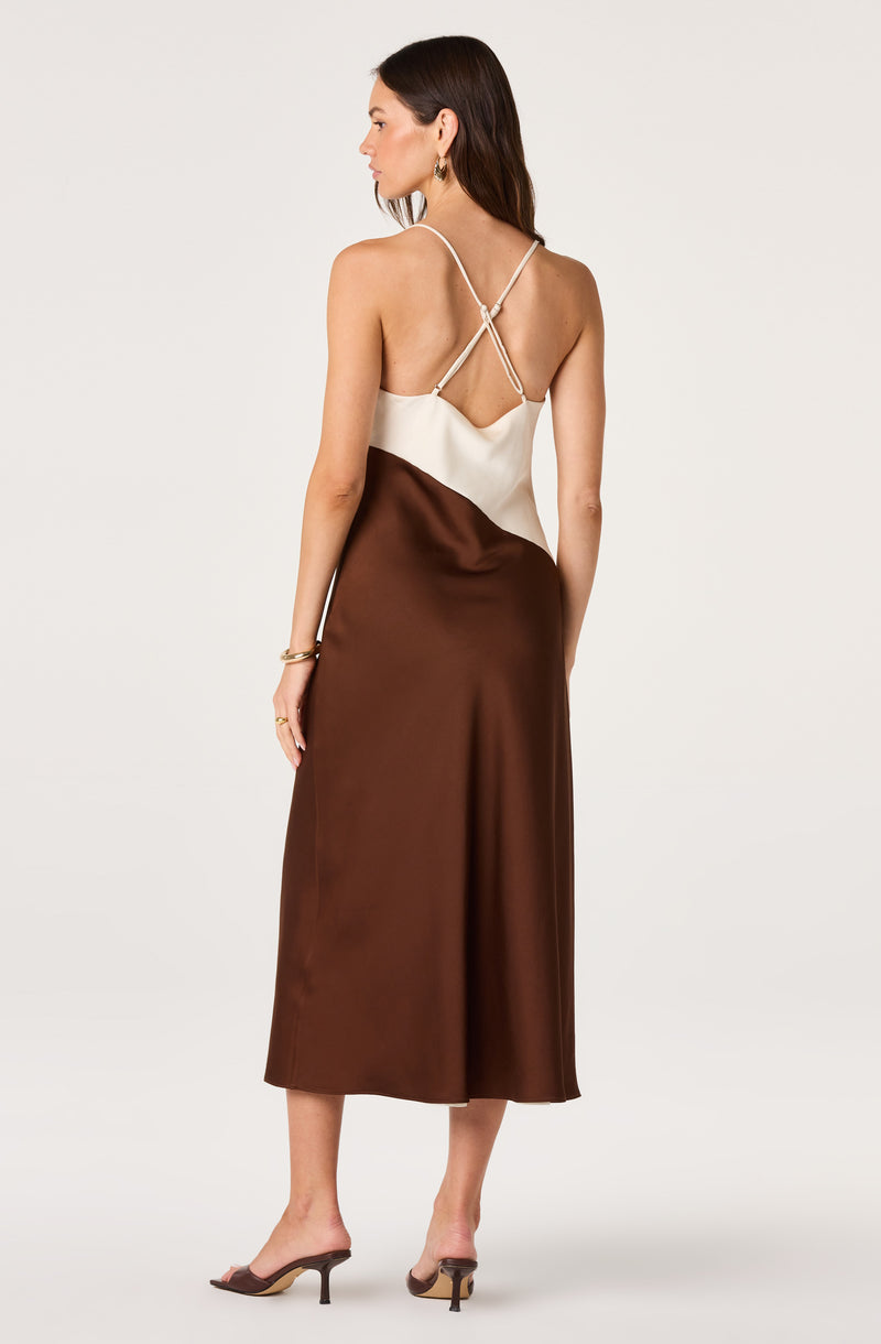 Woman in a satin brown and cream slip dress with thin, crisscross straps.