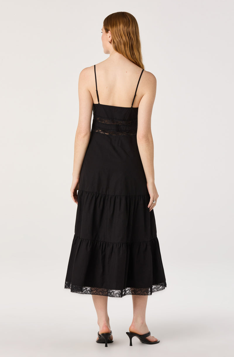 Woman in a black spaghetti strap dress with lace details and tiered skirt.