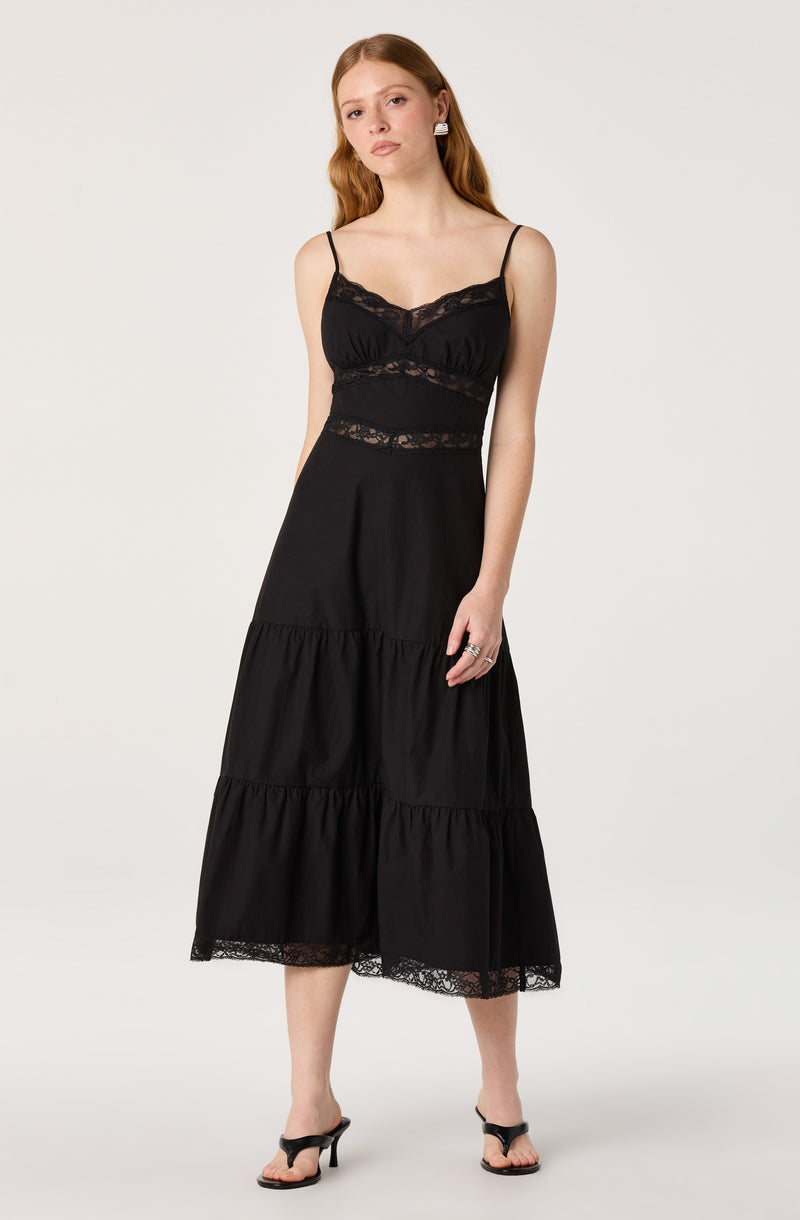 Woman wearing a black lace-trimmed spaghetti strap dress with tiered skirt.