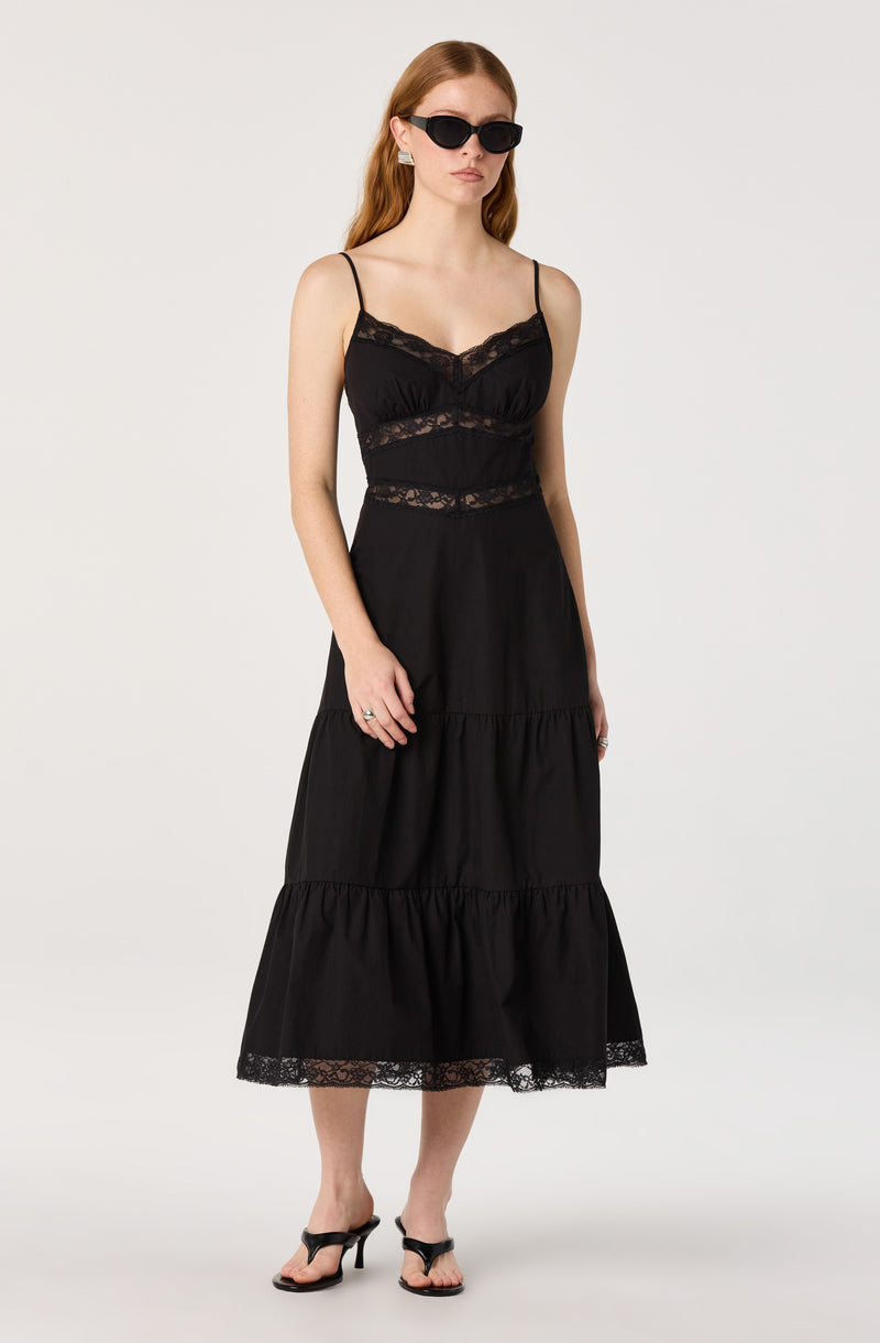 Woman in a black lace-trimmed sundress with spaghetti straps, wearing black sandals and sunglasses.
