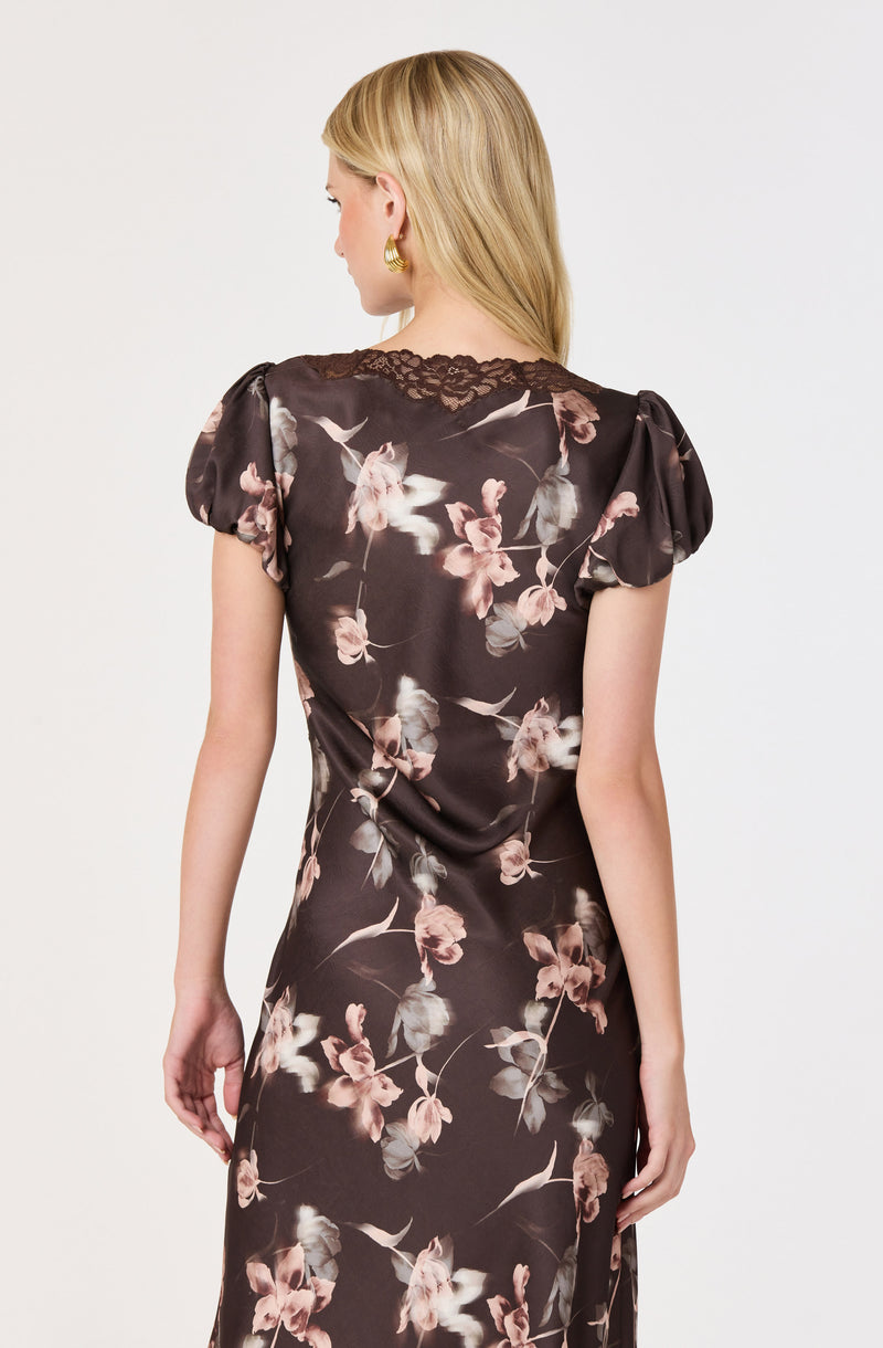 Woman in a dark floral dress with puff sleeves and lace accents at the shoulders.
