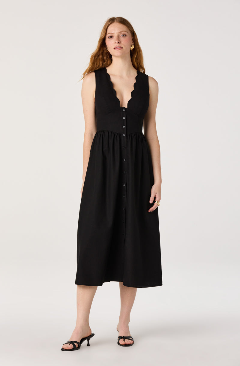 Woman in a black sleeveless, button-front dress with scalloped neckline and mid-calf length.