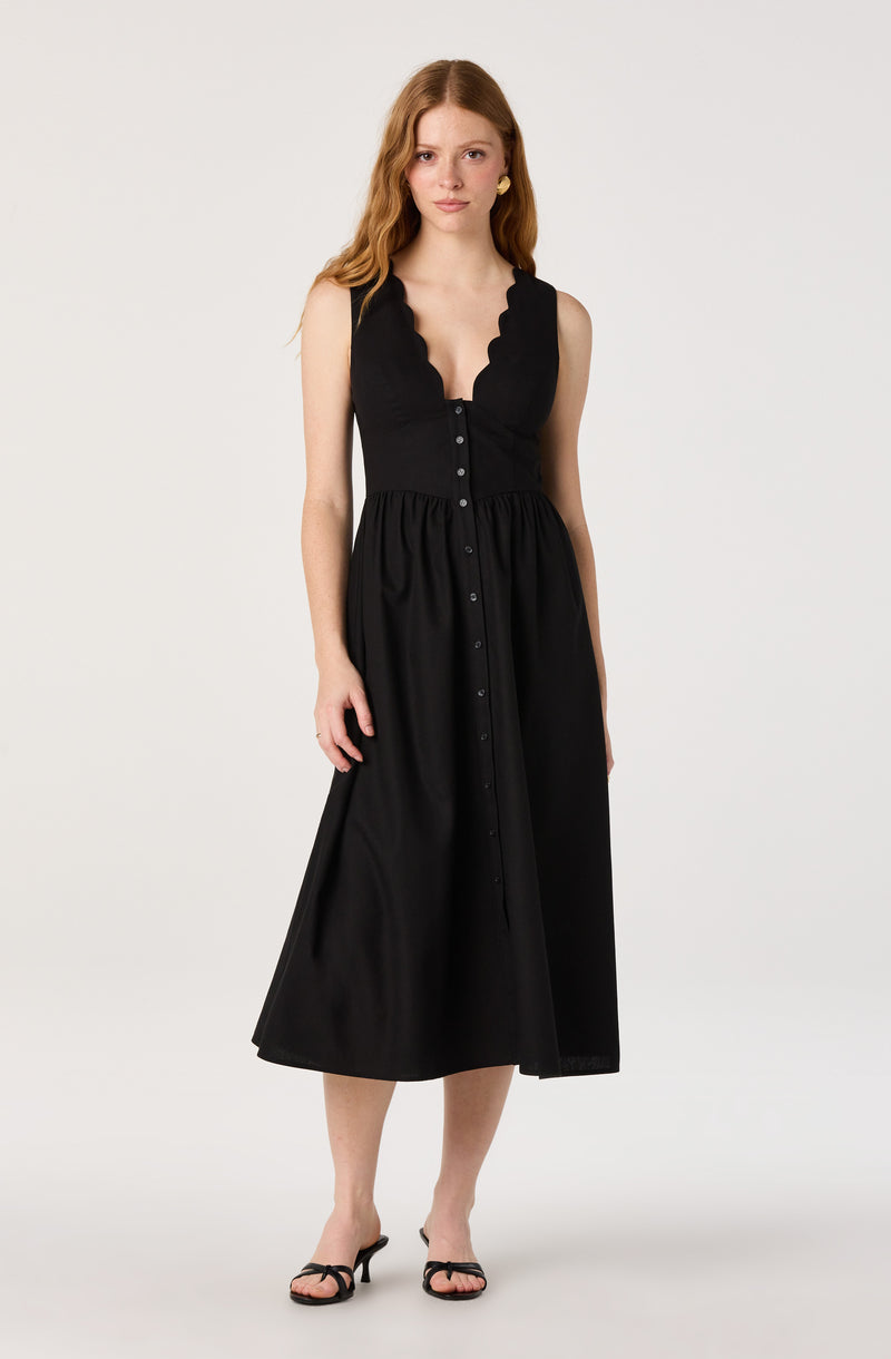Woman in a sleeveless black dress with scalloped neckline and button-down front.