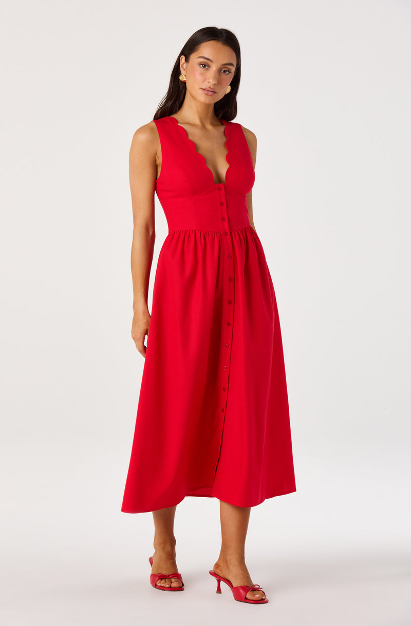 Woman wearing a sleeveless red dress with scalloped neckline and button-down front, paired with red heels.