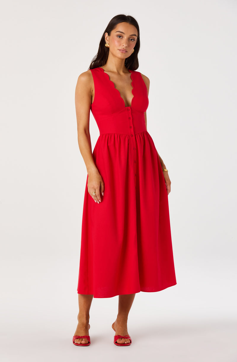 Woman wearing a sleeveless red dress with scalloped neckline and button-down skirt, paired with red heels.