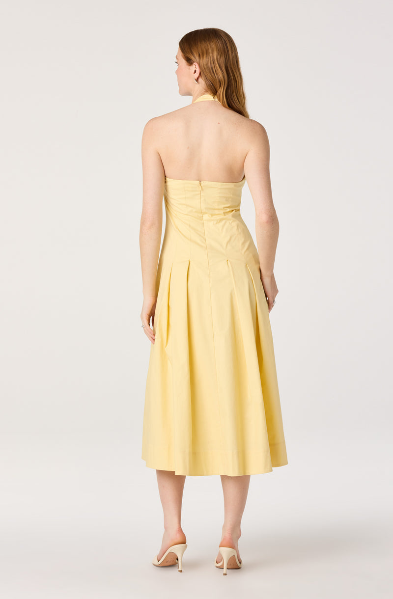 Back view of a woman in a strapless yellow dress with pleats and a fitted bodice, paired with beige heels.