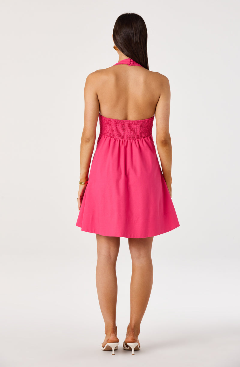 Back view of a woman wearing a strapless, pink halter-neck dress with a smocked waistband and flared skirt.