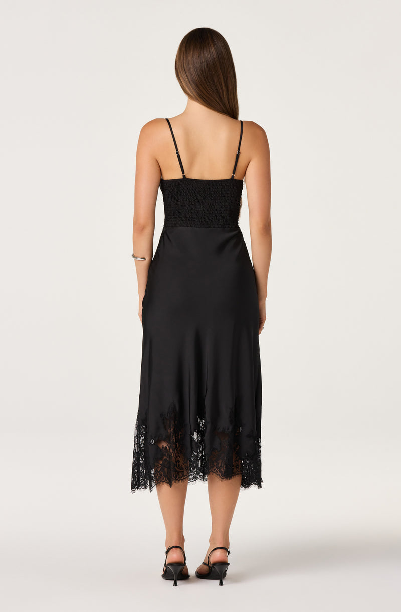 Woman in a black dress with spaghetti straps and lace trim at the hem.